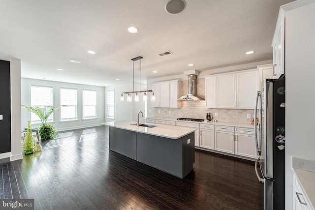 kitchen with dark wood-style flooring, decorative backsplash, freestanding refrigerator, a sink, and wall chimney exhaust hood