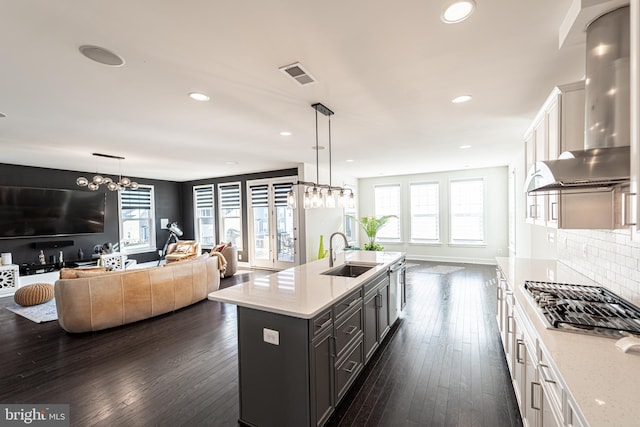 kitchen featuring stainless steel gas cooktop, a sink, visible vents, wall chimney range hood, and tasteful backsplash