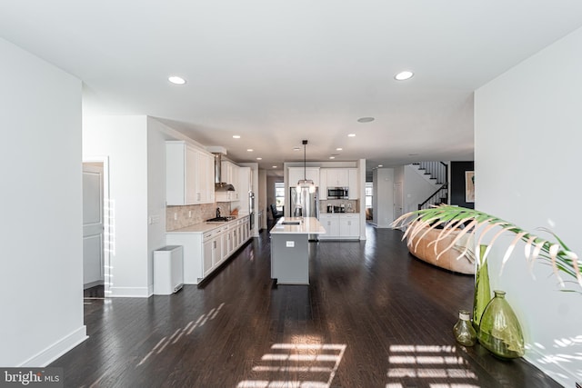 kitchen featuring white cabinets, dark wood finished floors, wall chimney exhaust hood, stainless steel appliances, and light countertops