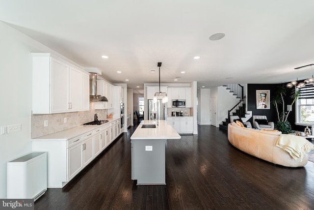 kitchen with stainless steel appliances, a sink, open floor plan, light countertops, and wall chimney exhaust hood