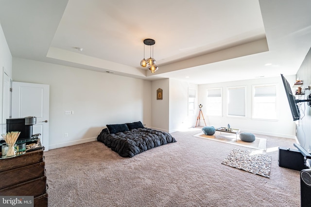 carpeted bedroom featuring a tray ceiling and baseboards