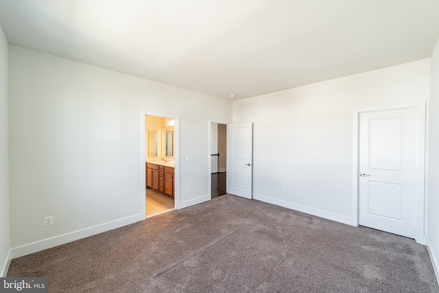 unfurnished bedroom featuring light colored carpet, ensuite bath, and baseboards