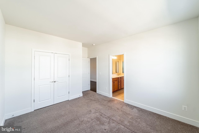 unfurnished bedroom featuring light carpet, a closet, connected bathroom, and baseboards