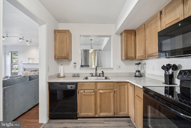 kitchen featuring light countertops, a sink, light wood finished floors, and black appliances