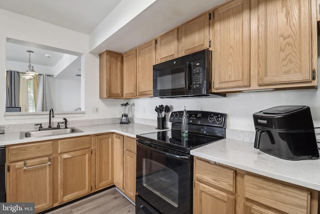 kitchen with black appliances, light countertops, a sink, and light wood finished floors