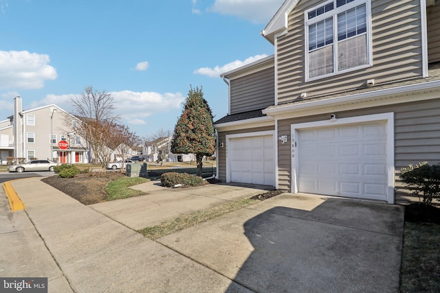 view of side of property with driveway, an attached garage, and a residential view