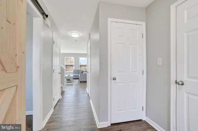 hallway featuring dark wood-style floors, a barn door, and baseboards