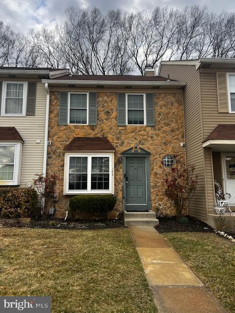 townhome / multi-family property with stone siding, a chimney, and a front yard