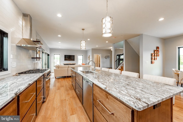 kitchen with stainless steel appliances, open floor plan, a sink, light wood-type flooring, and wall chimney exhaust hood