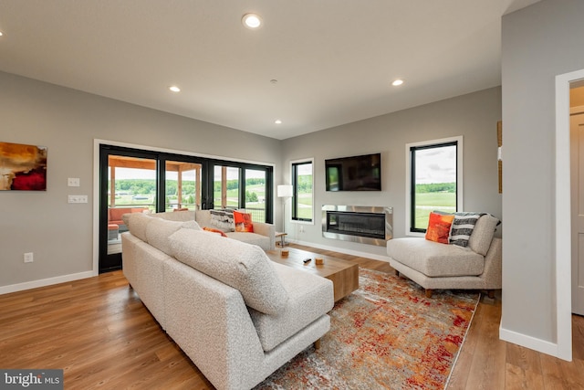 living room featuring baseboards, light wood-type flooring, a glass covered fireplace, and recessed lighting