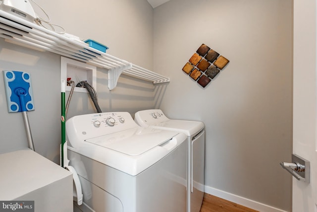 clothes washing area featuring laundry area, washer and clothes dryer, wood finished floors, and baseboards