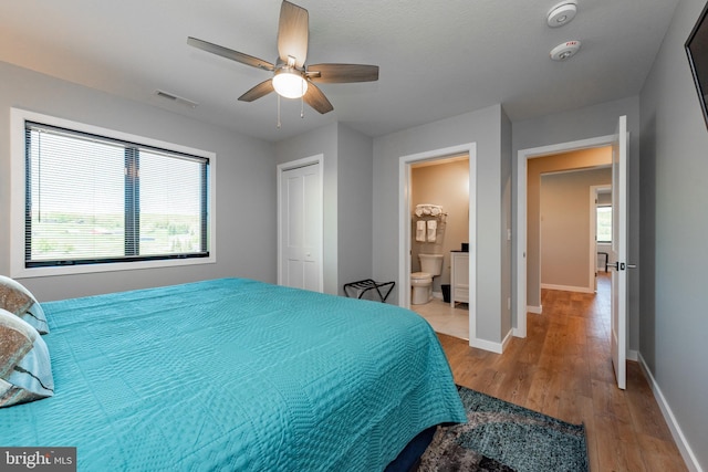 bedroom featuring visible vents, baseboards, ensuite bath, wood finished floors, and a closet