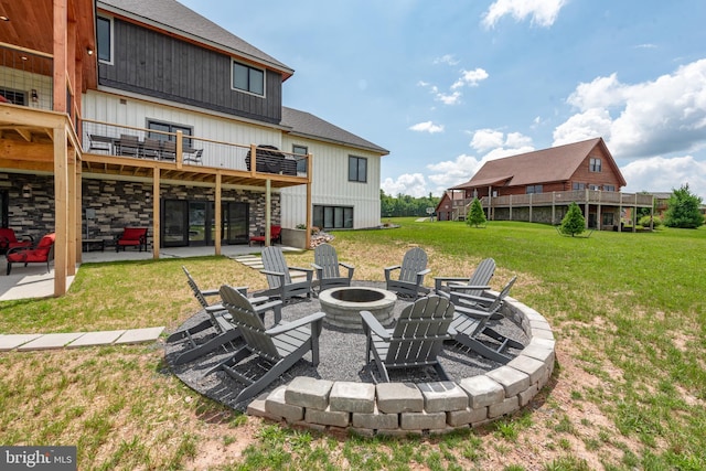 rear view of property with a fire pit, a lawn, a patio, stone siding, and roof with shingles