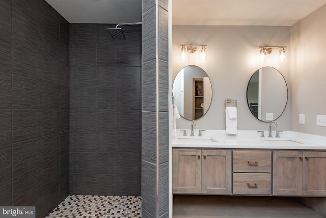 bathroom featuring double vanity, tiled shower, and a sink