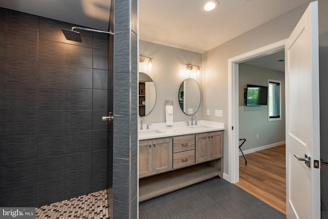 bathroom featuring a walk in shower, double vanity, a sink, and baseboards