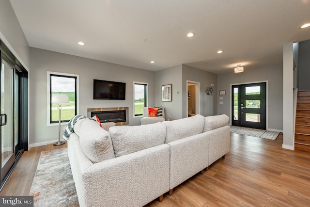 living room with recessed lighting, stairs, light wood-style flooring, and a glass covered fireplace