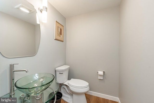 half bathroom with baseboards, a sink, toilet, and wood finished floors