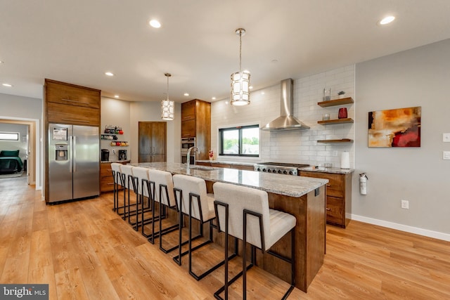 kitchen with wall chimney exhaust hood, appliances with stainless steel finishes, and brown cabinetry