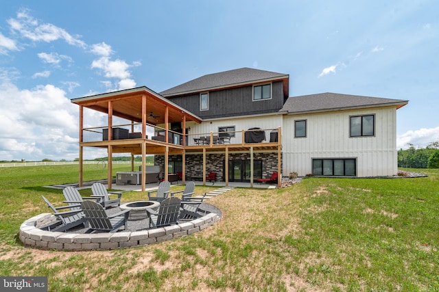 rear view of property with a fire pit, a patio area, a lawn, and a hot tub