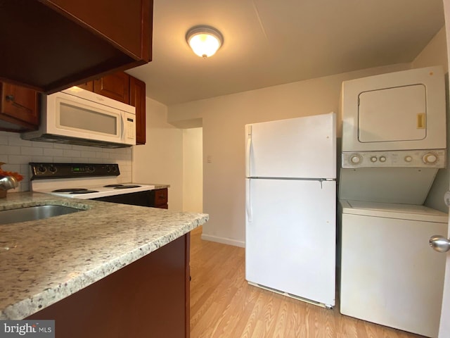 kitchen featuring stacked washer and dryer, light countertops, light wood-style flooring, decorative backsplash, and white appliances