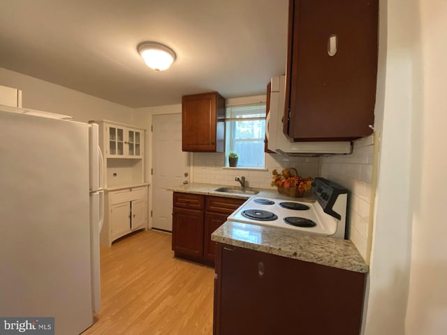 kitchen featuring light stone countertops, white appliances, a sink, light wood-style floors, and decorative backsplash