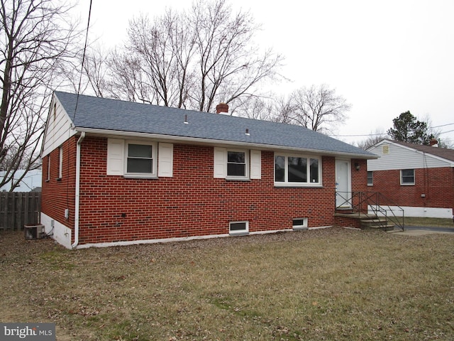 view of front of home with brick siding, a shingled roof, a chimney, fence, and a front yard