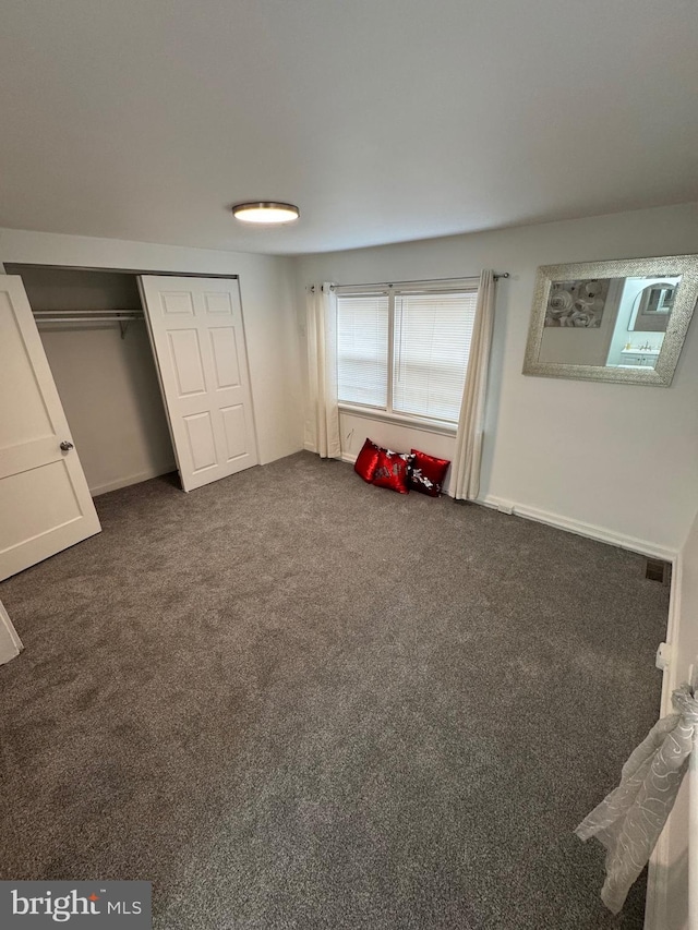 unfurnished bedroom with visible vents, dark colored carpet, and a closet