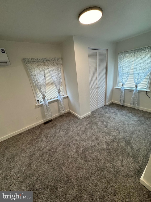 unfurnished bedroom with carpet floors, a closet, a wall mounted AC, and baseboards