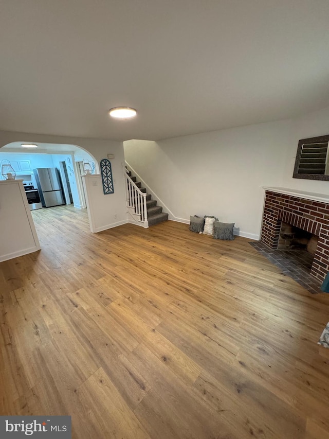 unfurnished living room featuring stairs, hardwood / wood-style floors, a fireplace, and arched walkways