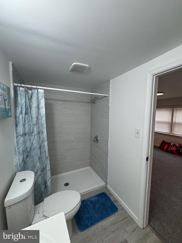 full bathroom with toilet, wood finished floors, a tile shower, and visible vents