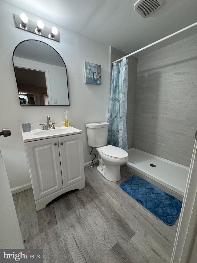 full bath with visible vents, toilet, wood finished floors, a tile shower, and vanity