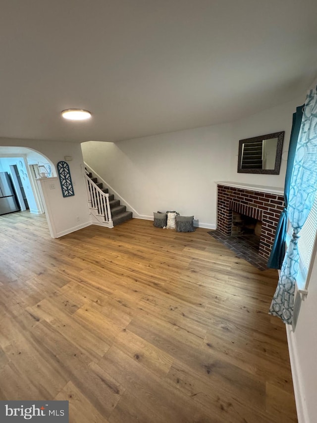 unfurnished living room featuring arched walkways, stairway, a fireplace, and wood finished floors