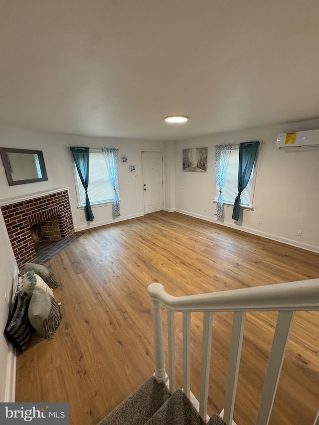 unfurnished living room with a brick fireplace, baseboards, wood finished floors, and a wall mounted AC