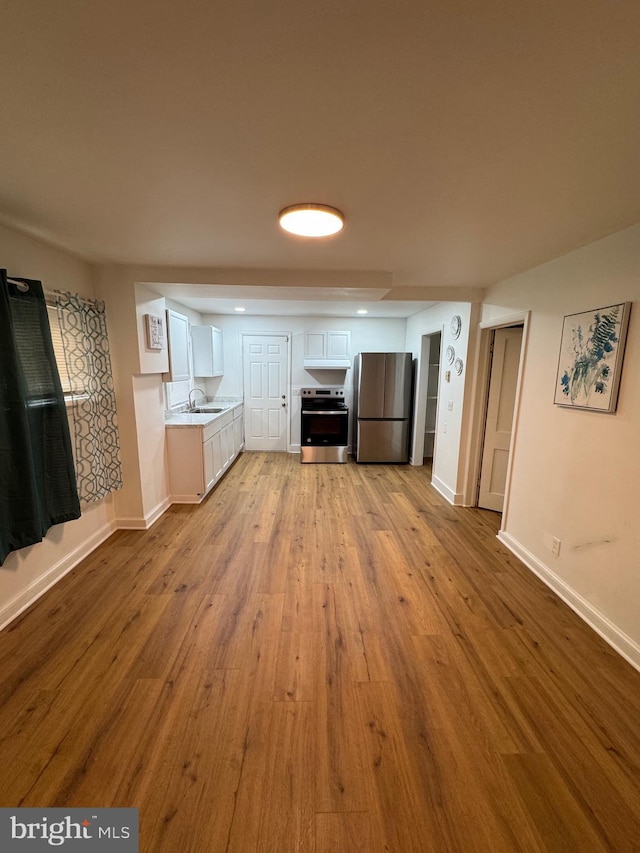 kitchen with a sink, stainless steel appliances, wood finished floors, and baseboards