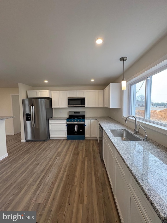 kitchen with light stone counters, dark wood-style floors, appliances with stainless steel finishes, white cabinetry, and a sink