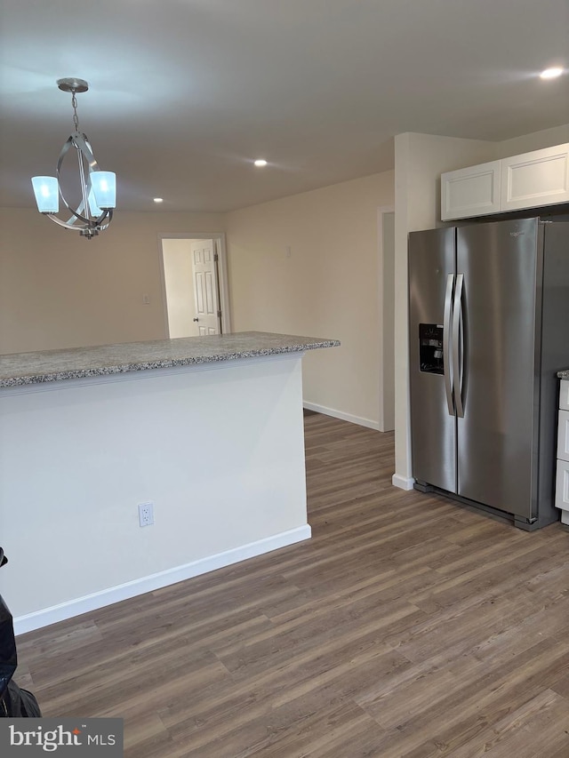 kitchen with stainless steel fridge, baseboards, white cabinets, wood finished floors, and decorative light fixtures