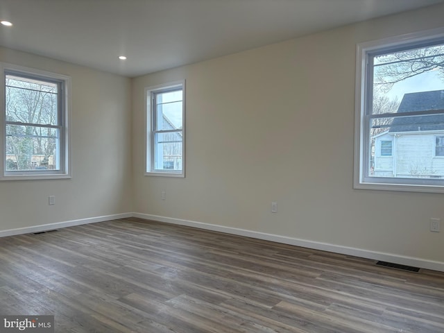 empty room with dark wood-style floors, visible vents, baseboards, and recessed lighting