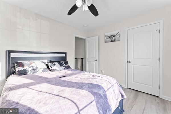 bedroom with a glass covered fireplace, ceiling fan, baseboards, and wood finished floors