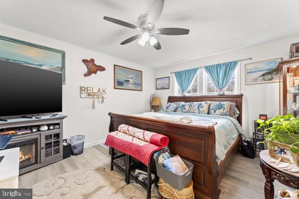 bedroom featuring ceiling fan, baseboards, wood finished floors, and a glass covered fireplace