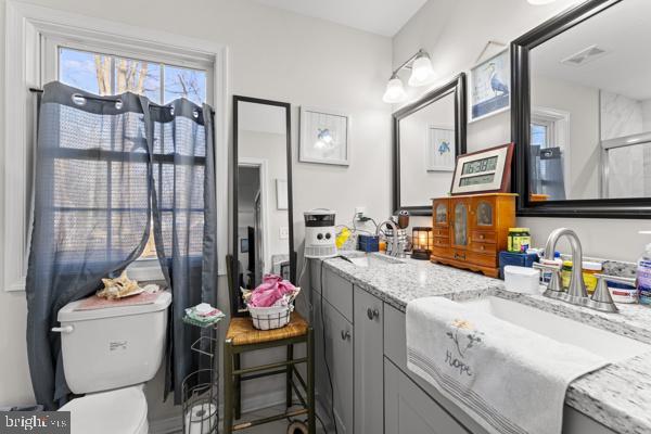 full bathroom with double vanity, visible vents, toilet, and a sink