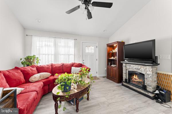 living area featuring a ceiling fan, vaulted ceiling, a stone fireplace, and wood finished floors