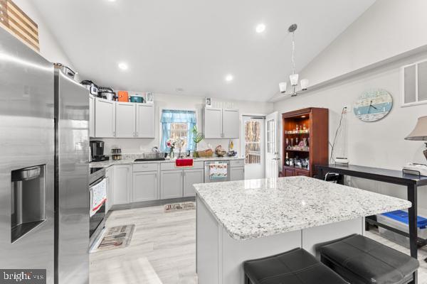 kitchen featuring lofted ceiling, light stone counters, stainless steel appliances, a center island, and a kitchen bar