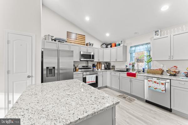 kitchen with lofted ceiling, appliances with stainless steel finishes, a sink, light stone countertops, and light wood-type flooring