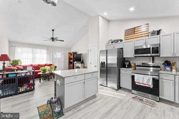 kitchen with appliances with stainless steel finishes, a center island, light wood-style floors, and a ceiling fan