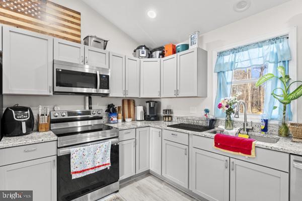 kitchen with lofted ceiling, light stone counters, stainless steel appliances, and a sink