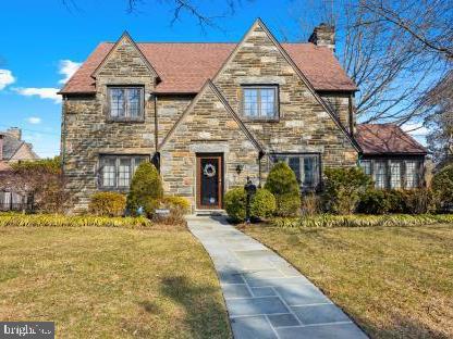 english style home featuring stone siding, a chimney, and a front yard