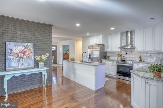 kitchen with wood finished floors, visible vents, stainless steel appliances, white cabinetry, and wall chimney range hood