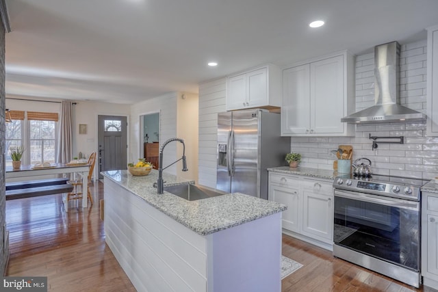 kitchen featuring a sink, stainless steel appliances, wood finished floors, and wall chimney range hood