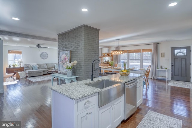 kitchen with light stone countertops, white cabinetry, dark wood finished floors, a sink, and stainless steel dishwasher