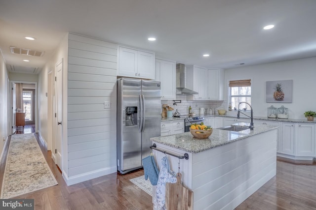 kitchen featuring visible vents, a sink, wall chimney range hood, appliances with stainless steel finishes, and dark wood-style flooring